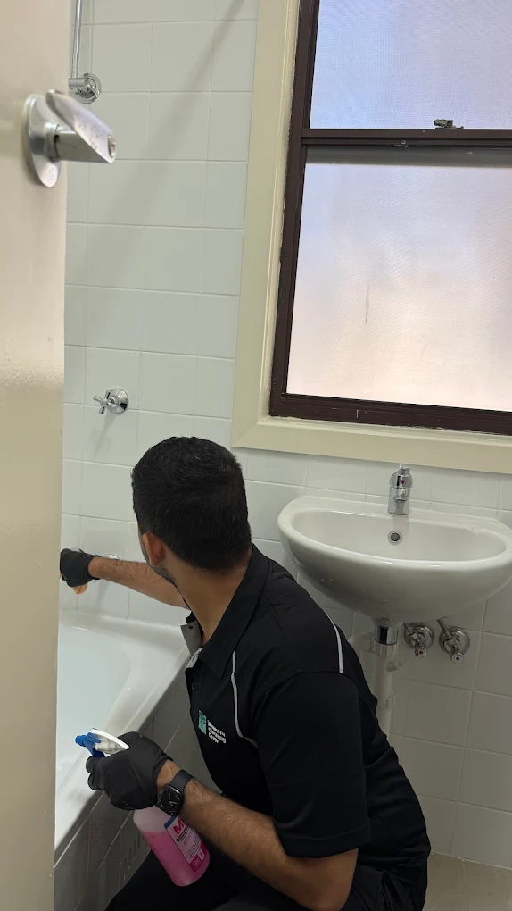 Cleaner scrubbing a bathtub and tiled wall in a tenant bathroom