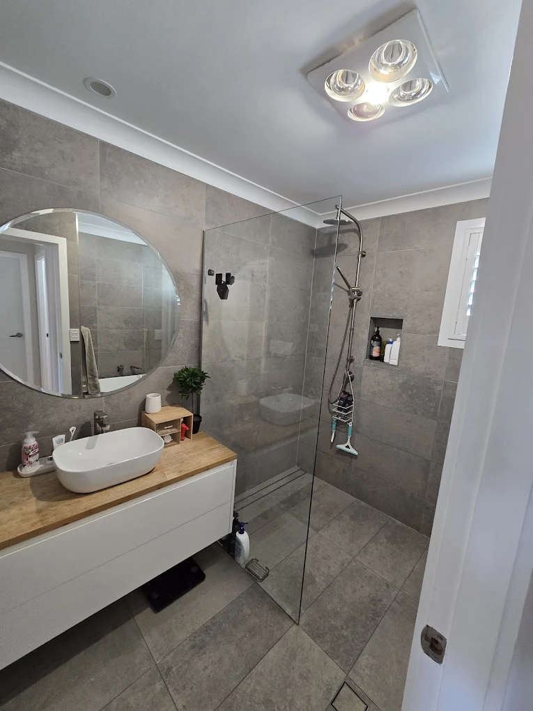 Grey-tiled ensuite with round mirror, timber vanity and walk-in shower after professional clean